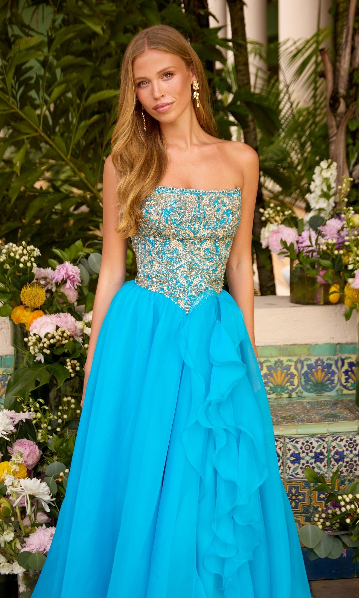 The Ava Presley 47420 is a turquoise strapless floor-length ball gown featuring a bodice with intricate gold embroidery and a matching full, ruffled skirt.